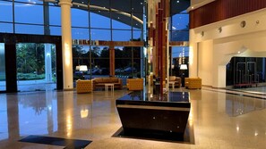 Un lobby espacioso con un mostrador de recepción negro central, zonas de estar cómodas y grandes ventanales con vistas al exterior.