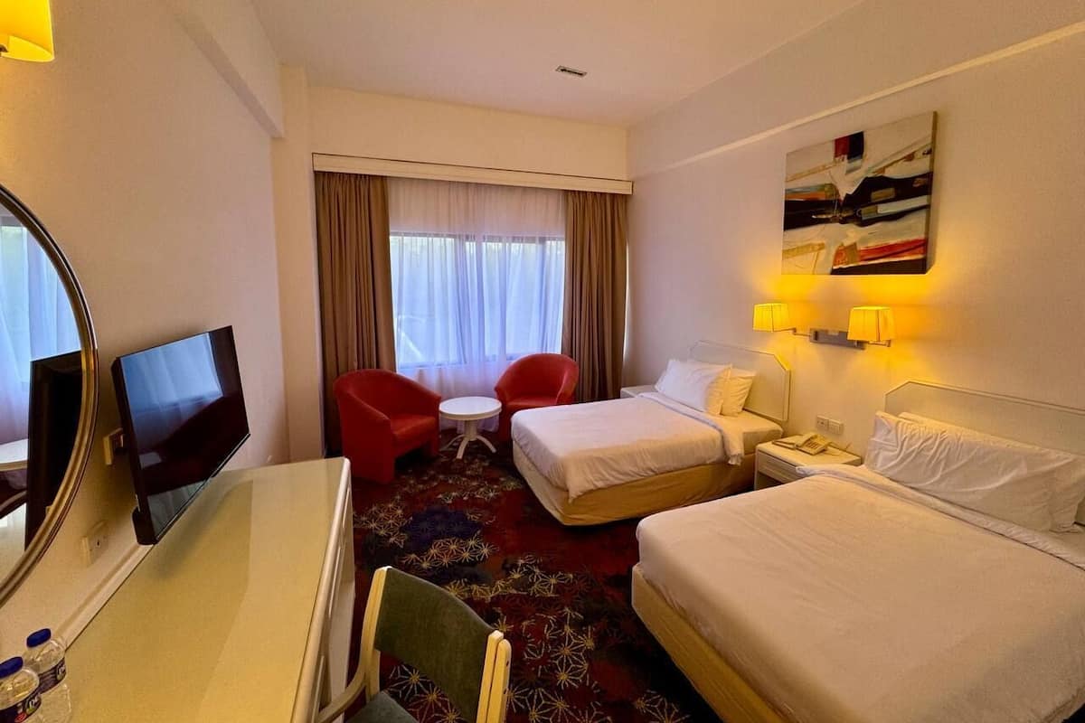 Une chambre d’hôtel avec deux lits, un bureau avec une télévision, une petite table et deux chaises.