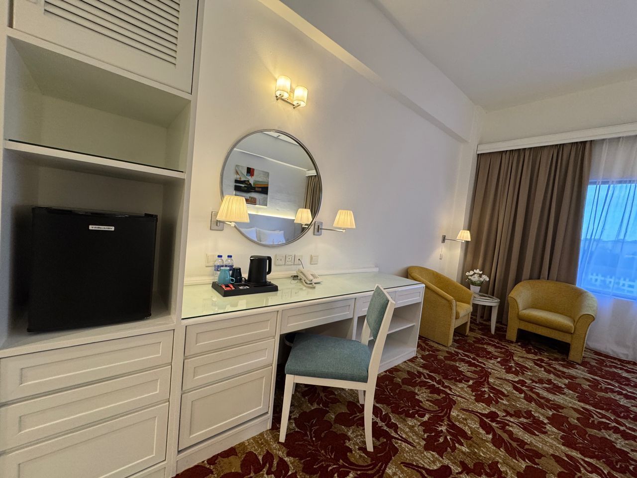 A hotel room with a desk, chair, television, and a large mirror.