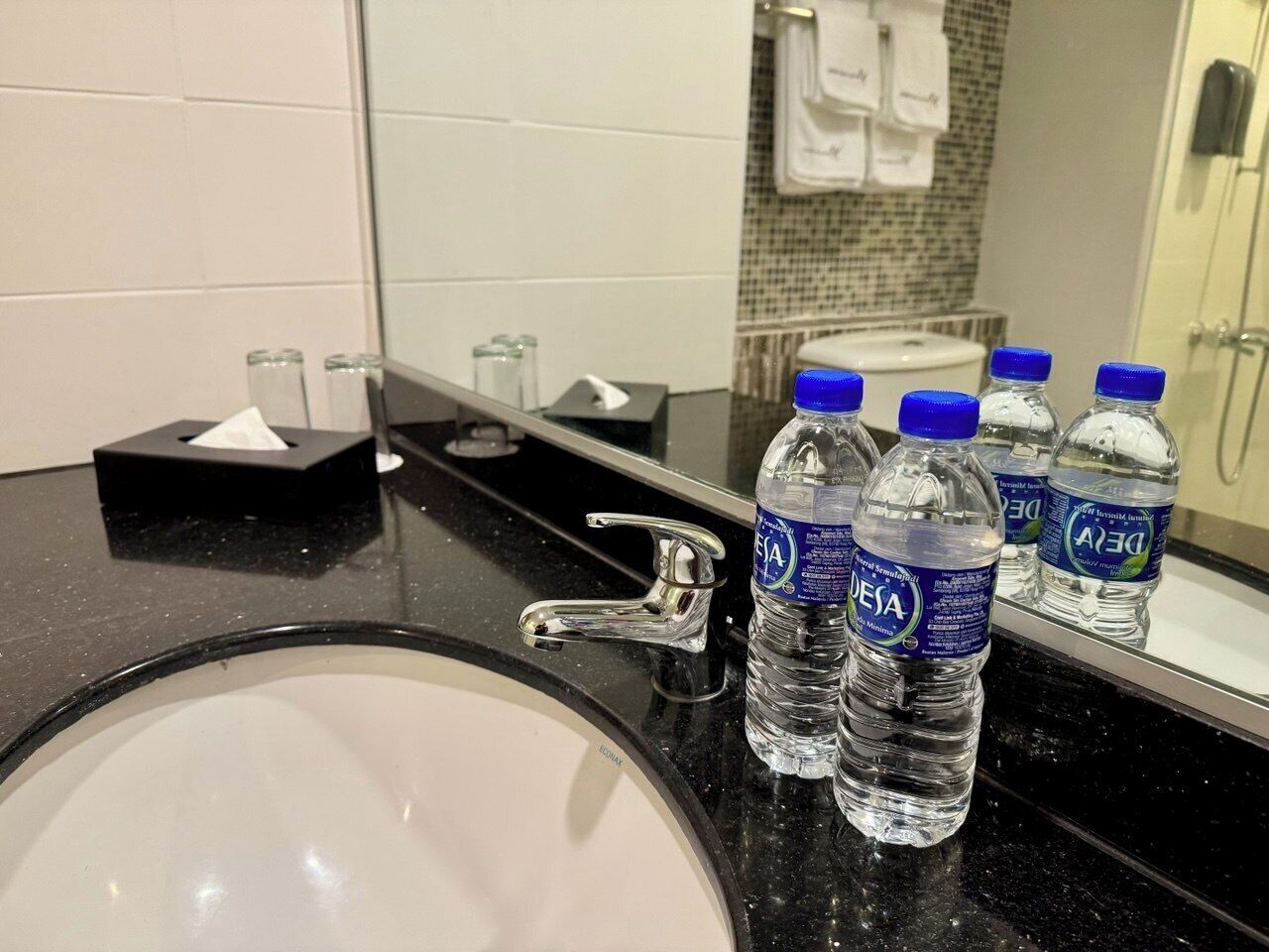 A hotel bathroom with a sink, faucet, and several bottles of water labeled 'DEJA'.
