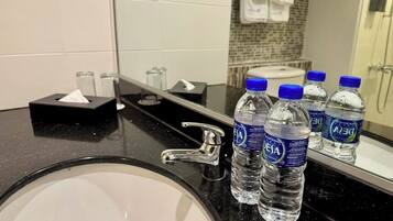 A hotel bathroom with a sink, faucet, and several bottles of water labeled 'DEJA'.