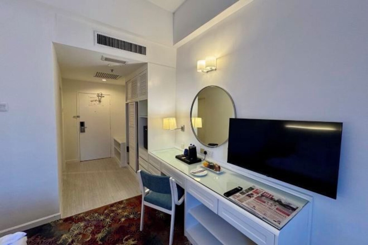 A hotel room with a flat-screen TV, a desk with a chair, a mirror, and a door leading to another room.