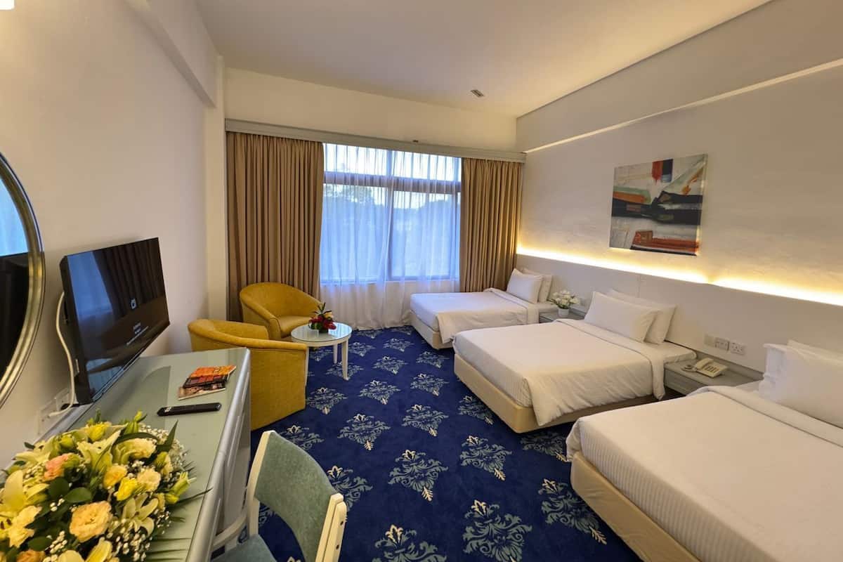 Une chambre d’hôtel avec deux lits, un bureau avec une télévision, une chaise et une petite table agrémentée de fleurs.