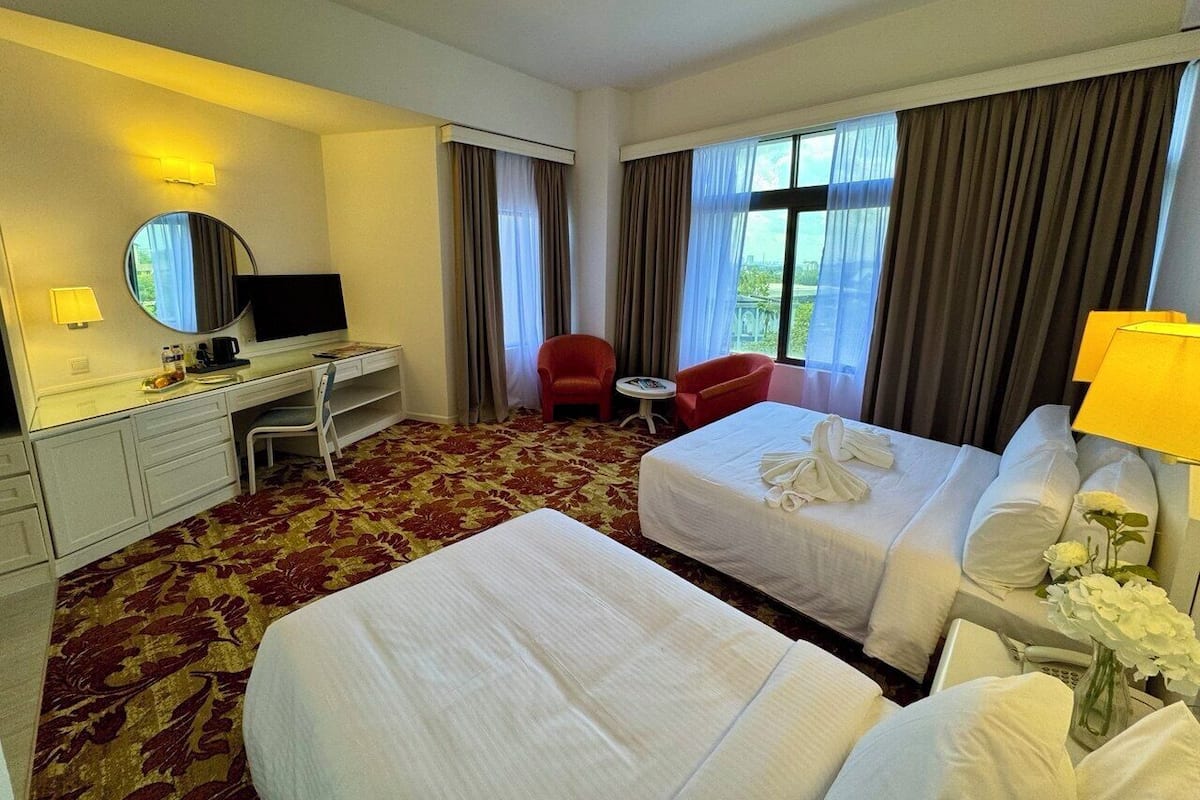 Une chambre d’hôtel avec deux lits, un bureau avec une chaise, une télévision et un fauteuil rouge.