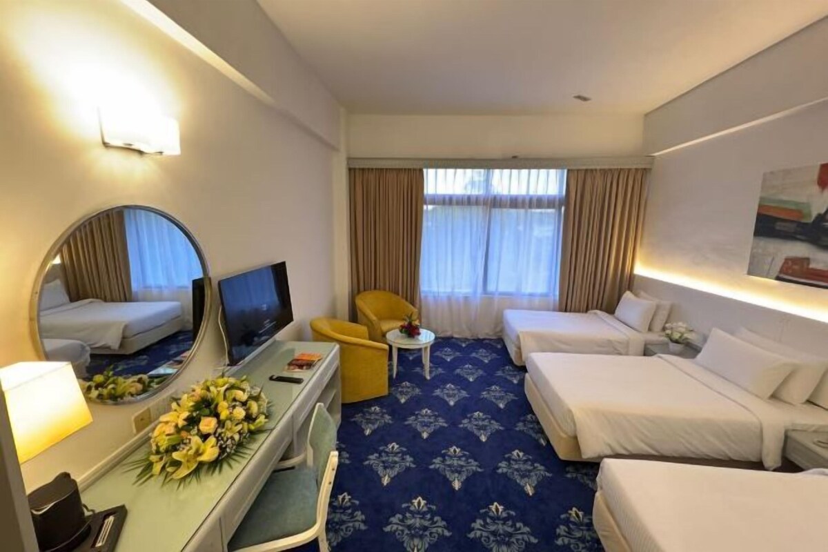 Une chambre d’hôtel comprenant un lit, un bureau avec une chaise, une petite table, un canapé, un miroir et une fenêtre avec des rideaux.