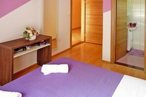 A hotel room with a bed, a wooden desk, a bathroom with a shower, and a purple mat on the floor. - House in Starigrad near Paklenica Park (Starigrad Paklenica)