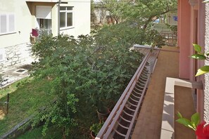 A balcony with a view of a garden and a building with a window and shutters. - House in Starigrad near Paklenica Park (Starigrad Paklenica)