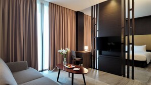 Ein Hotelzimmer mit einer Couch, einem Esstisch mit Blumenvase, einem Fernseher und einem Bett.
