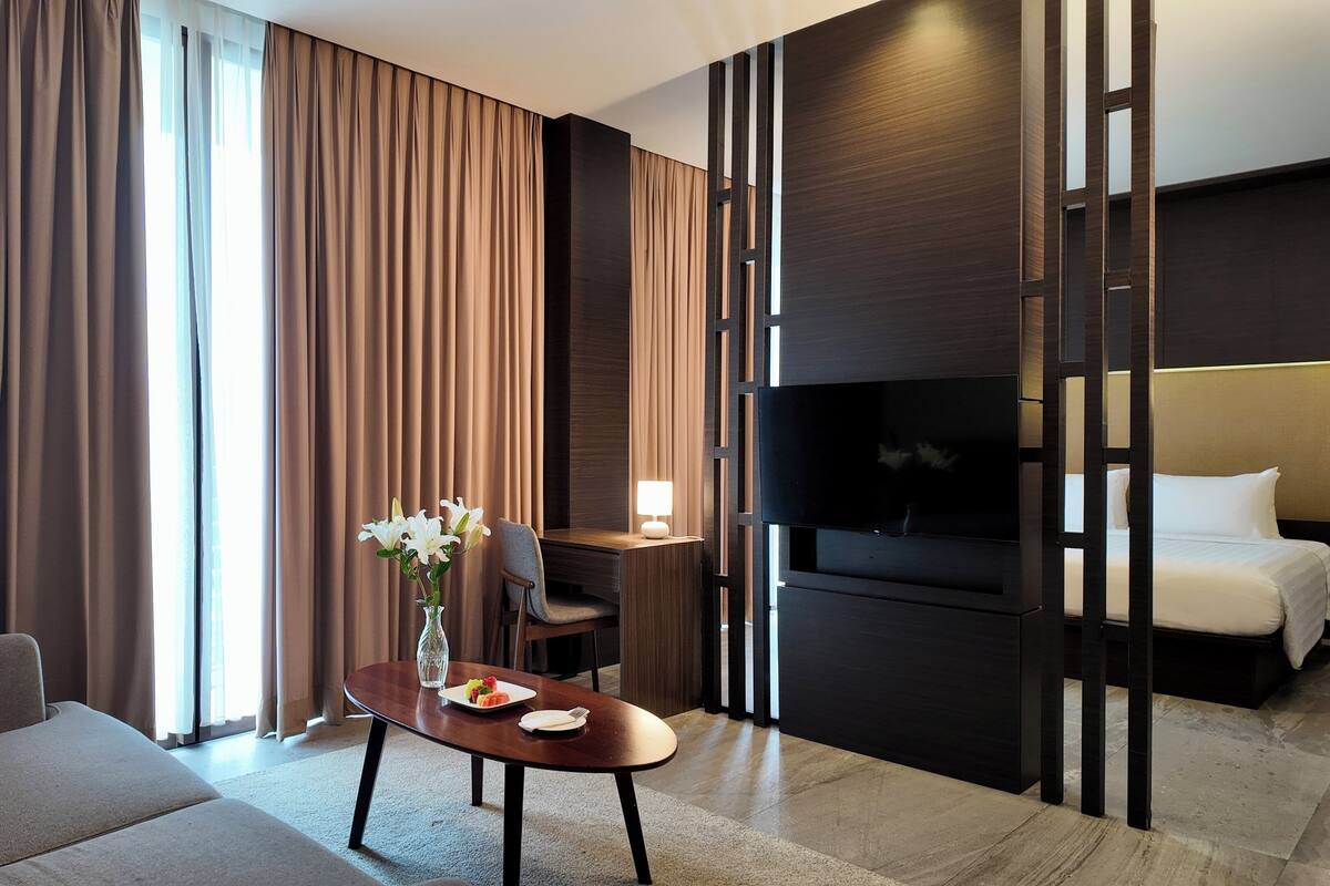 Ein Hotelzimmer mit einer Couch, einem Esstisch mit Blumenvase, einem Fernseher und einem Bett.