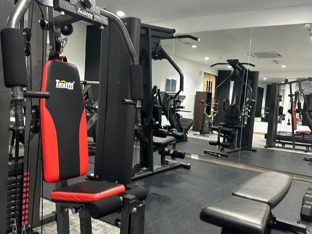 Une salle de sport équipée de divers appareils d’exercice, notamment un banc de musculation rouge et noir et un support à squats.