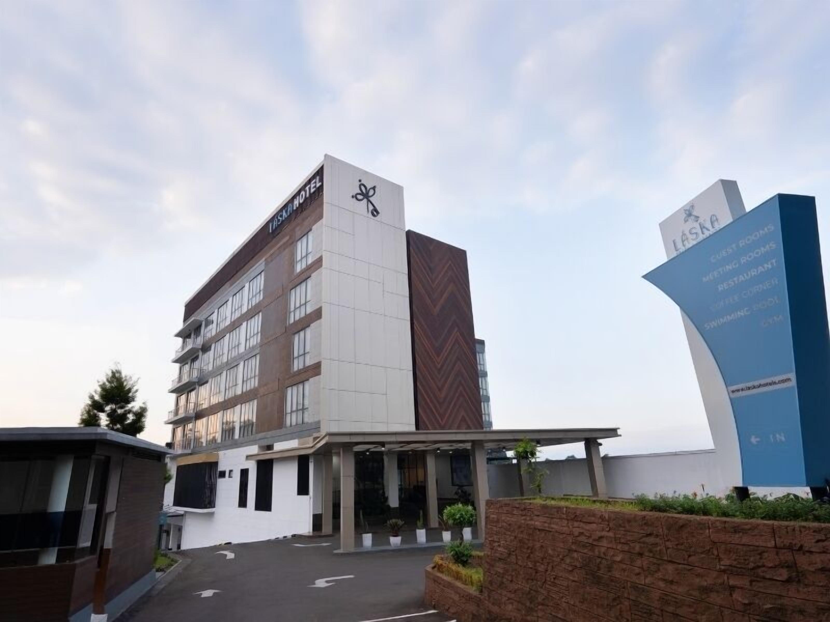 A modern hotel with a prominent sign indicating amenities such as guest rooms, meeting rooms, a restaurant, coffee corner, swimming pool, and gym.