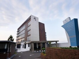 Un hotel moderno con un cartel llamativo que indica servicios como habitaciones para huéspedes, salas de reuniones, restaurante, rincón de café, piscina y gimnasio.
