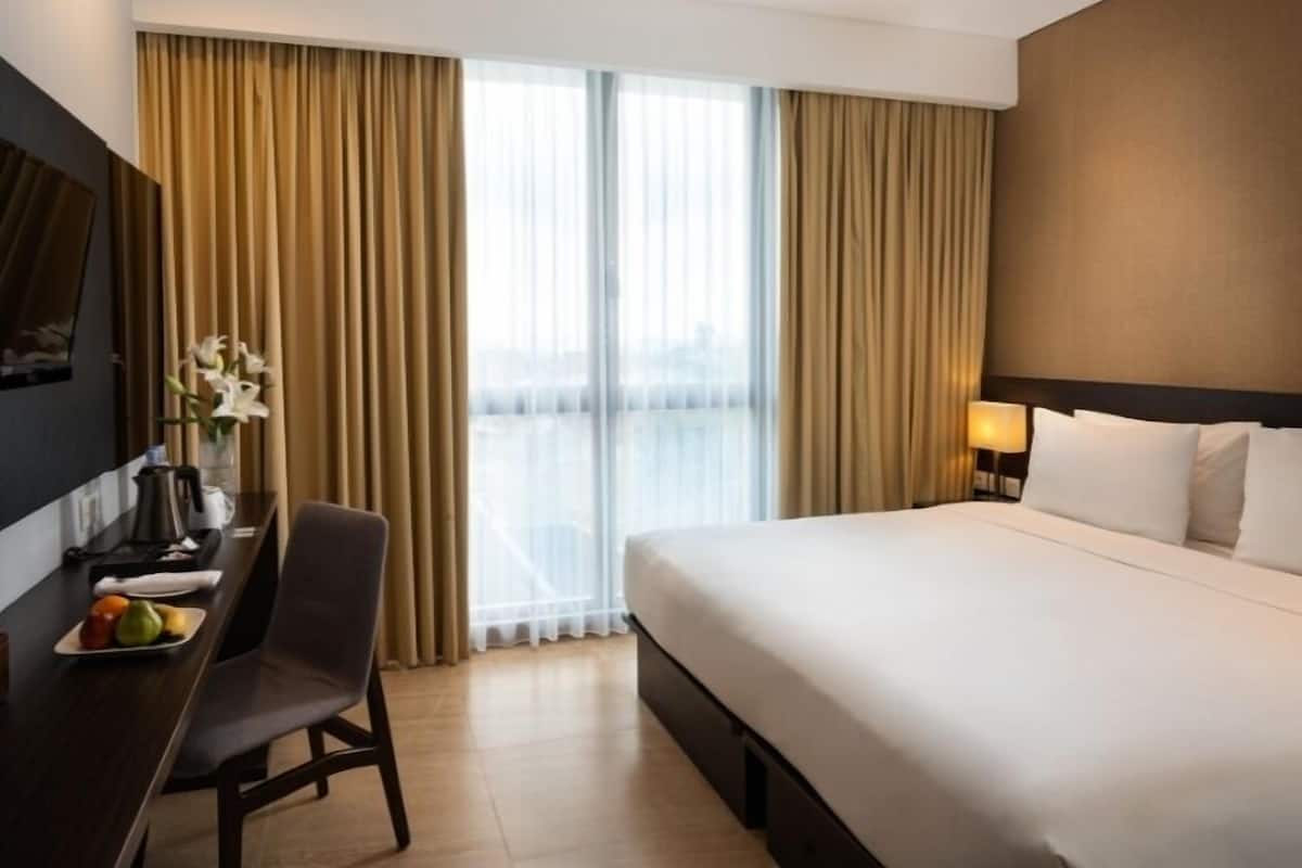 Ein Hotelzimmer mit einem großen Bett, einem Schreibtisch mit Stuhl, einem Fernseher und einem Fenster mit Vorhängen.