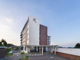 Un edificio moderno con un logotipo destacado en la fachada, una zona de acceso cubierta y un estacionamiento con flechas direccionales.