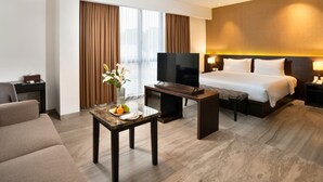 A hotel room with a bed, a TV, a desk with a vase of flowers, and a sofa. - Laska Hotel Sukabumi (Sukabumi)