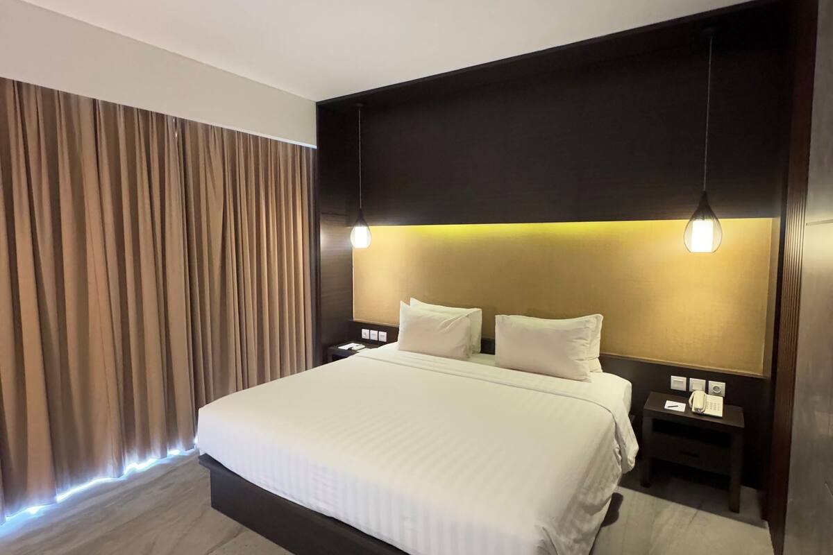 Ein modernes Hotelzimmer mit einem großen Bett, einem dunklen Kopfteil und stimmungsvoller Beleuchtung.