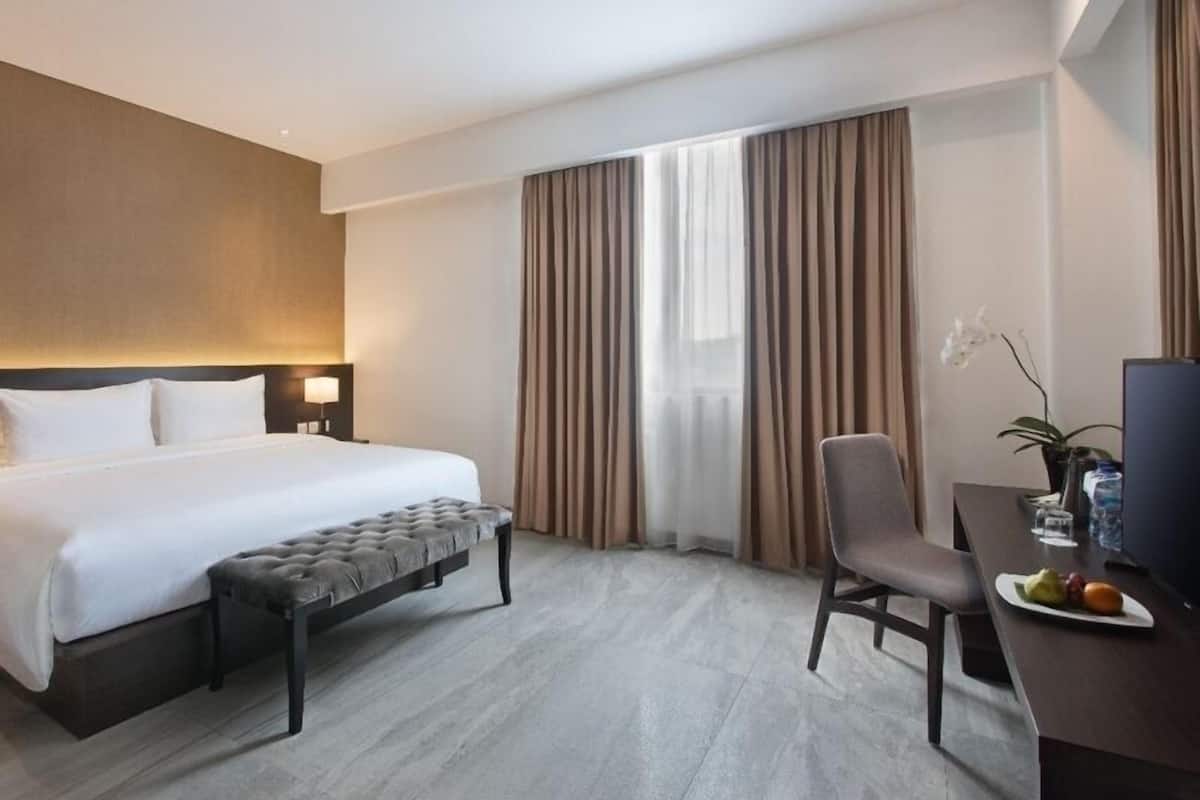 Ein Hotelzimmer mit Bett, Schreibtisch mit Stuhl, Fernseher und einem Fenster mit Vorhängen.