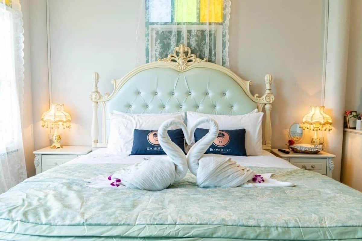 Una cama con cabecera capitonada, dos almohadas con un logotipo y dos almohadas con forma de cisne.
