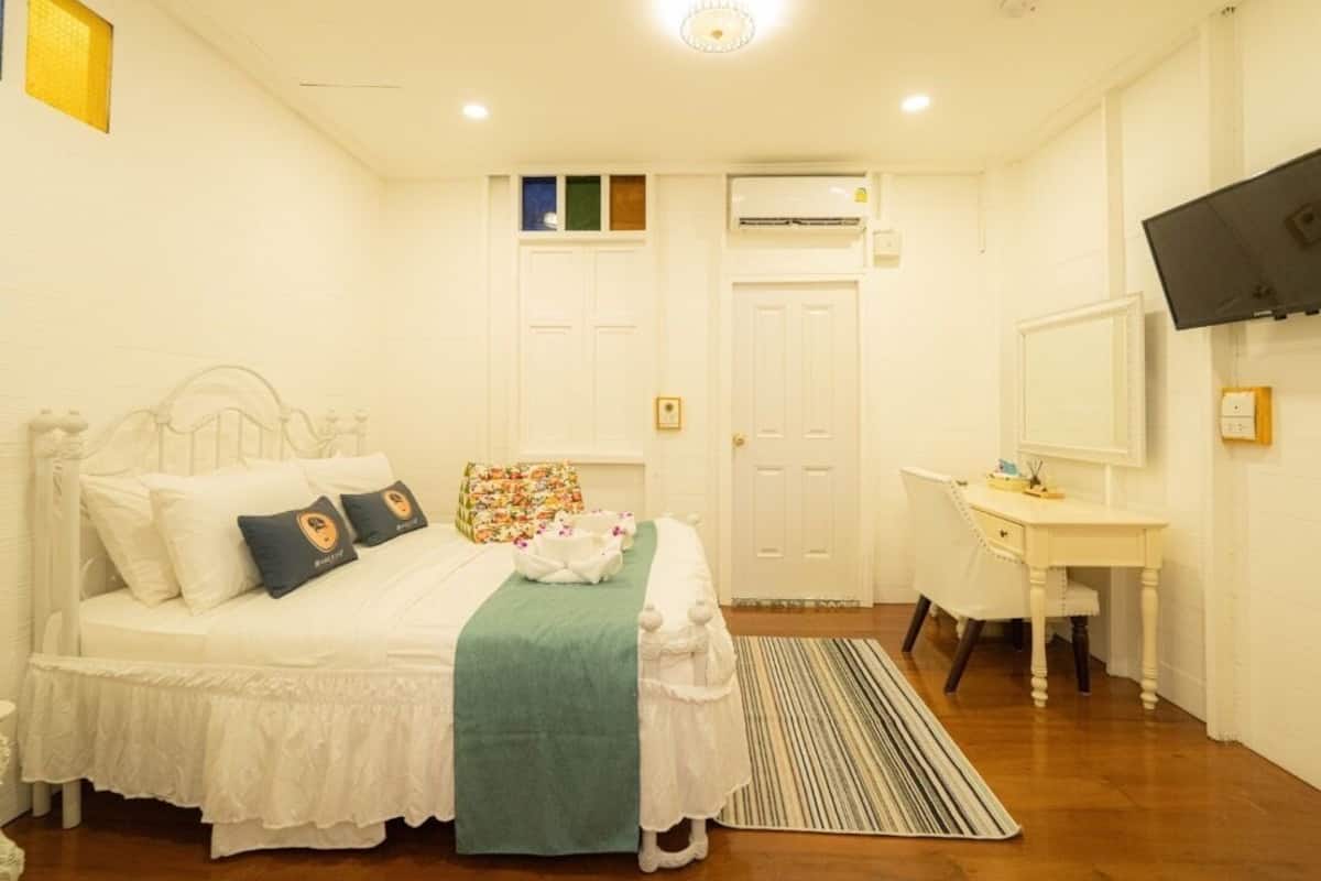 Un dormitorio con cama, mesita de noche, escritorio y televisor en la pared.