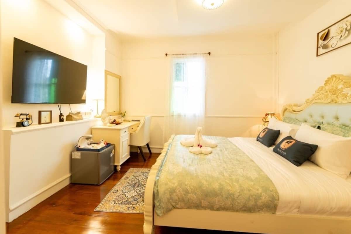 Un dormitorio con cama, escritorio, televisor y ventana con cortinas.