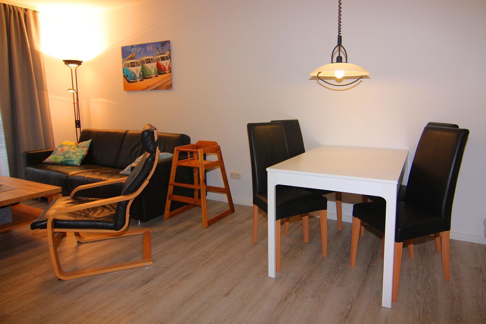A living room with a sofa, two rocking chairs, a dining table with chairs, a floor lamp, and a hanging light fixture.