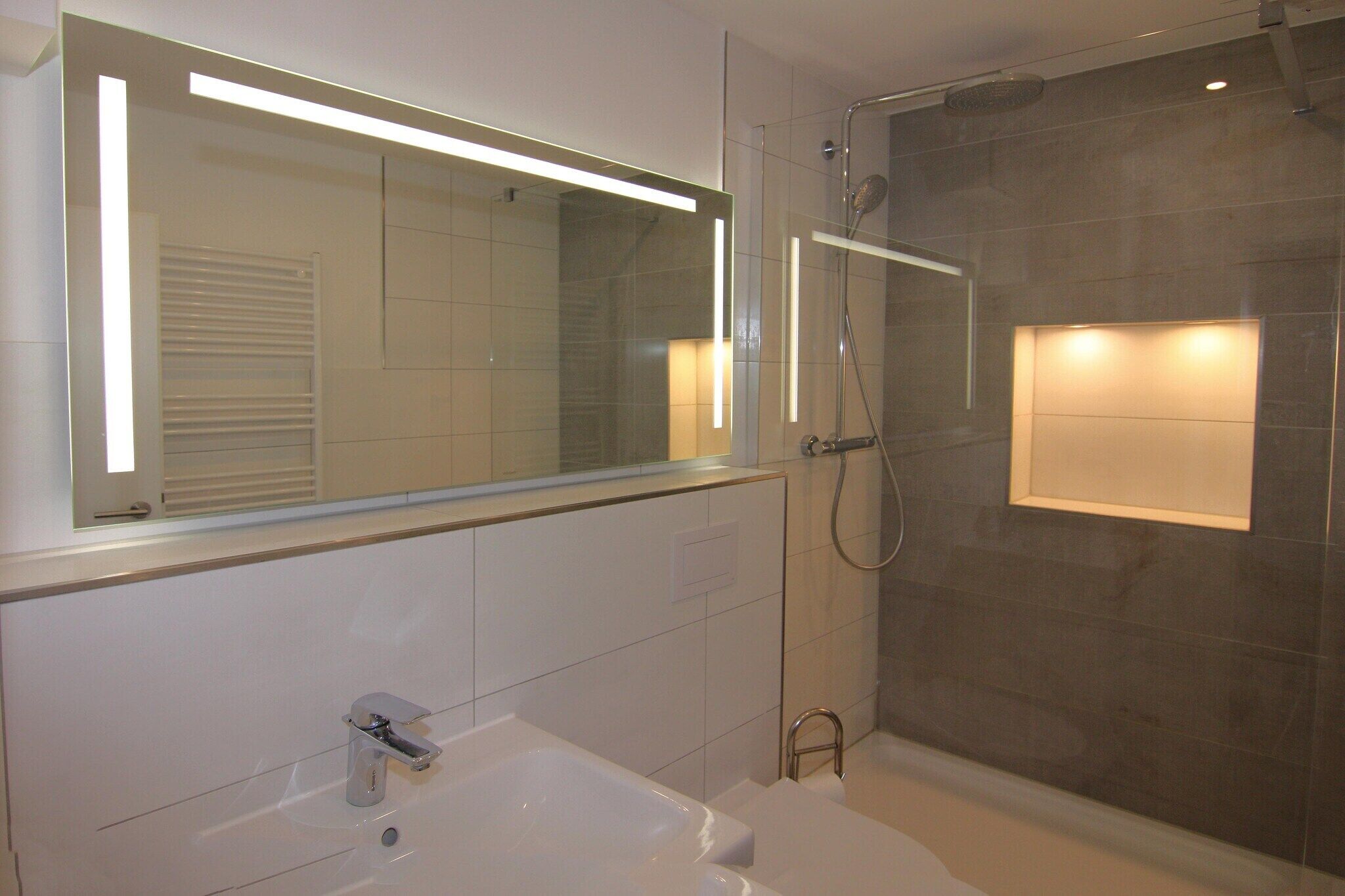 A modern bathroom with a large mirror, a bathtub, and a shower.