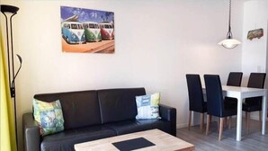 A living room with a black sofa, a wooden coffee table, and a dining area with a white table and black chairs. - Ferienwohnung auf Fehmarn in Orther Reede (Orth)