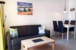 A living room with a black sofa, a wooden coffee table, and a dining area with a white table and black chairs.