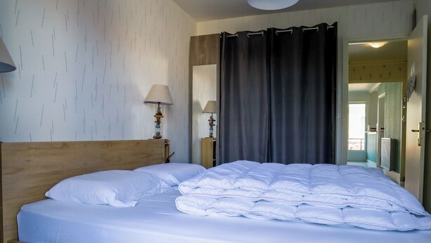 Een opgemaakt bed met witte lakens, een houten hoofdbord en twee bedlampjes.