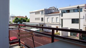 Een balkon met uitzicht op een straat, een rode auto en een wit gebouw met een balkon.
