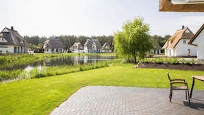A residential area with houses, a pond, and a paved patio with a chair. - Komfortables Ferienhaus mit Sauna in Fuhlendorf (Fuhlendorf)