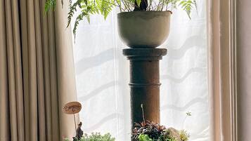 Una habitación con un ventanal grande, un helecho en maceta y una planta pequeña sobre un pedestal.