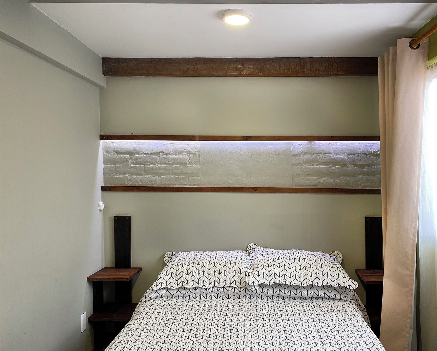 A bedroom with a bunk bed, wooden beams, a white brick wall, and a bed with patterned bedding.