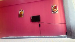 A room with pink walls, a bed with a patterned bedspread, a flat-screen TV mounted on the wall, and two wall decorations. - Hotel Delux (Mwanza)
