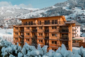 Un edificio de madera de varios pisos con balcones, rodeado de árboles cubiertos de nieve y un paisaje montañoso.