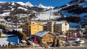 Une station de montagne où les bâtiments sont recouverts de neige, notamment un chalet en bois remarquable et un hôtel moderne doté de balcons.