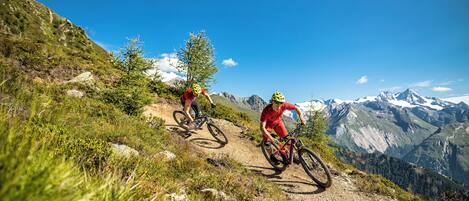 Twee mountainbikers op een onverharde pad met een bergachtige achtergrond.