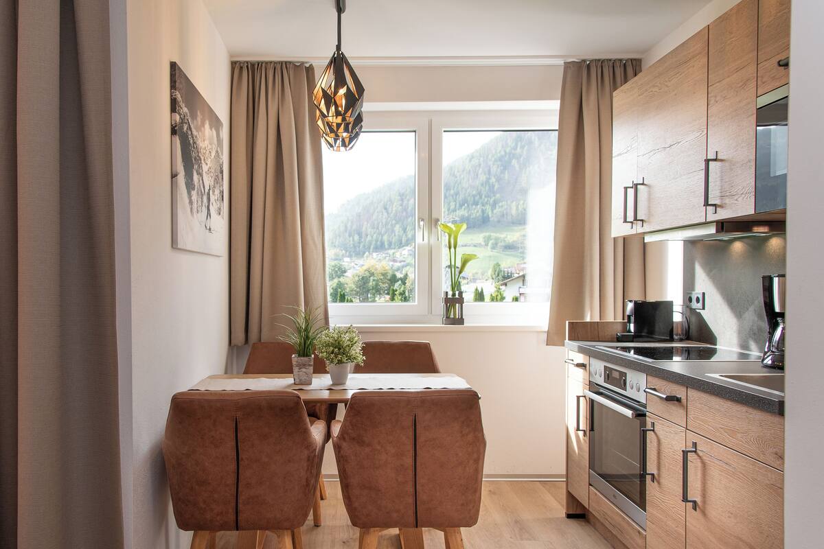 Eine moderne Küche mit Holdekor, einem Esstisch mit zwei Stühlen und einem Fenster mit Blick auf eine Berglandschaft.