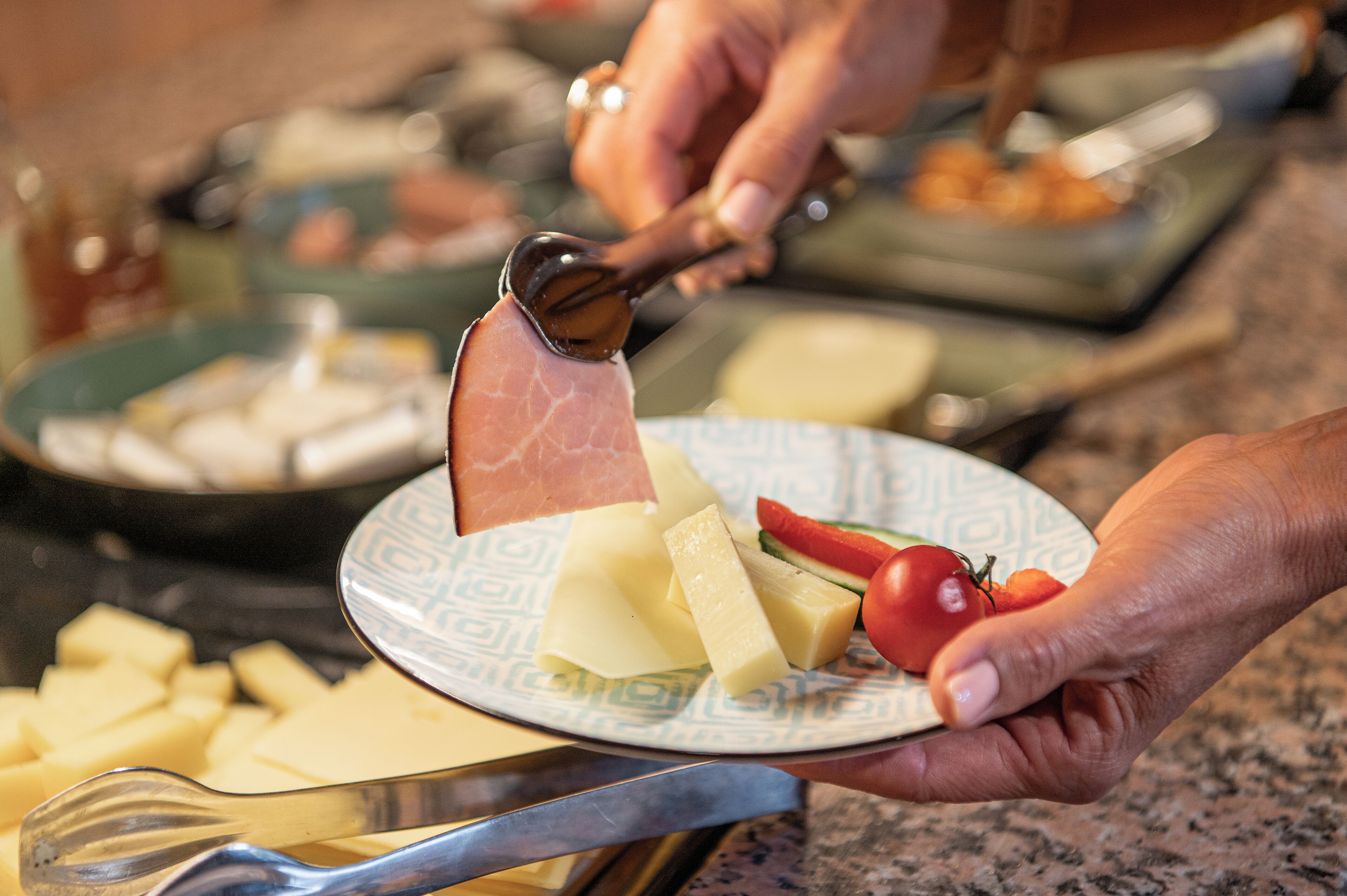 A plate with cheese, ham, and a tomato.