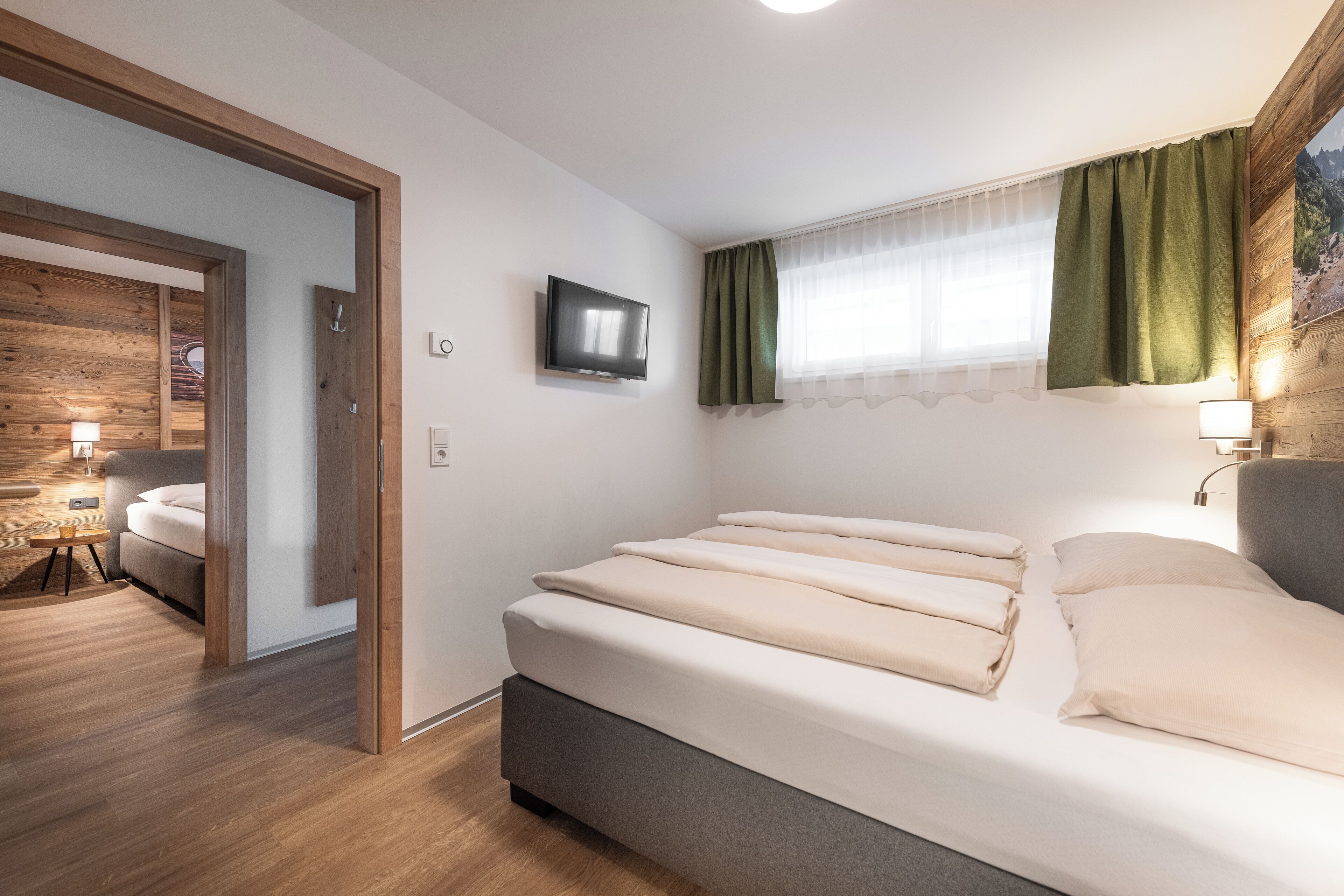 A modern bedroom with a bed, a television, and a window with curtains.