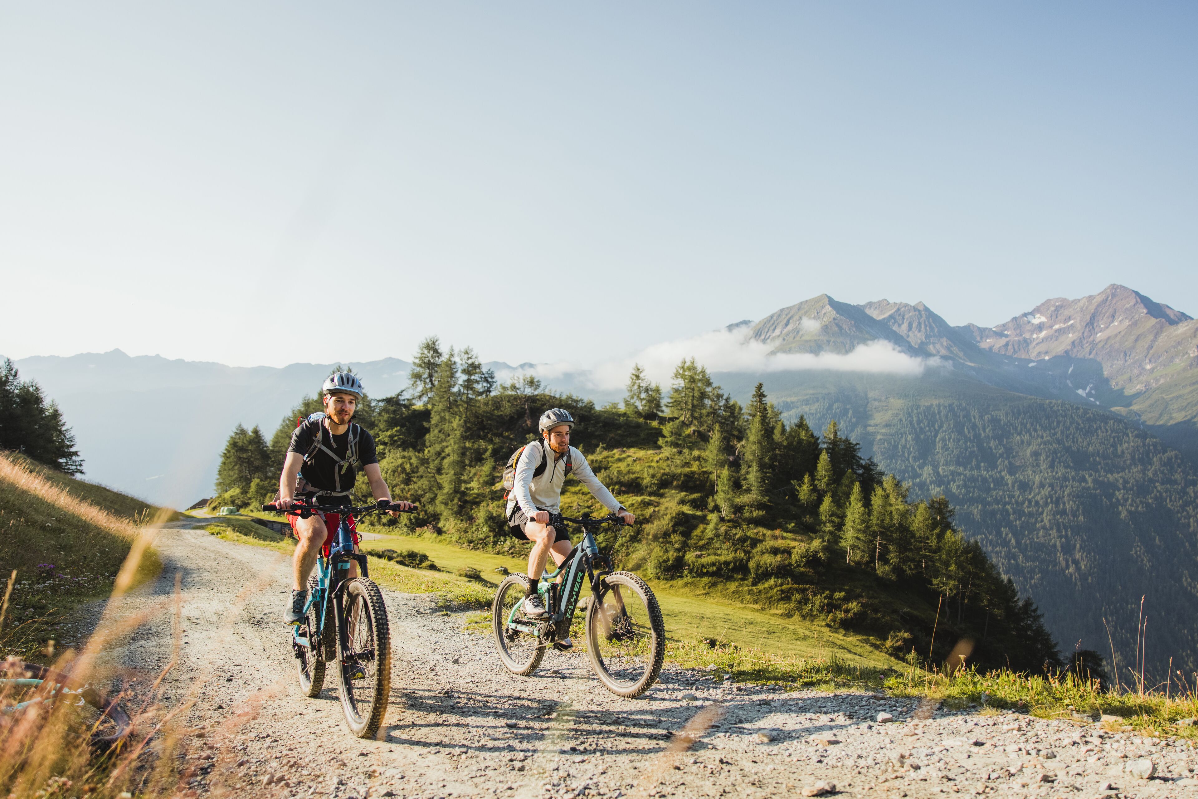Two cyclists on a mountain trail with a clear view of the surrounding landscape.
