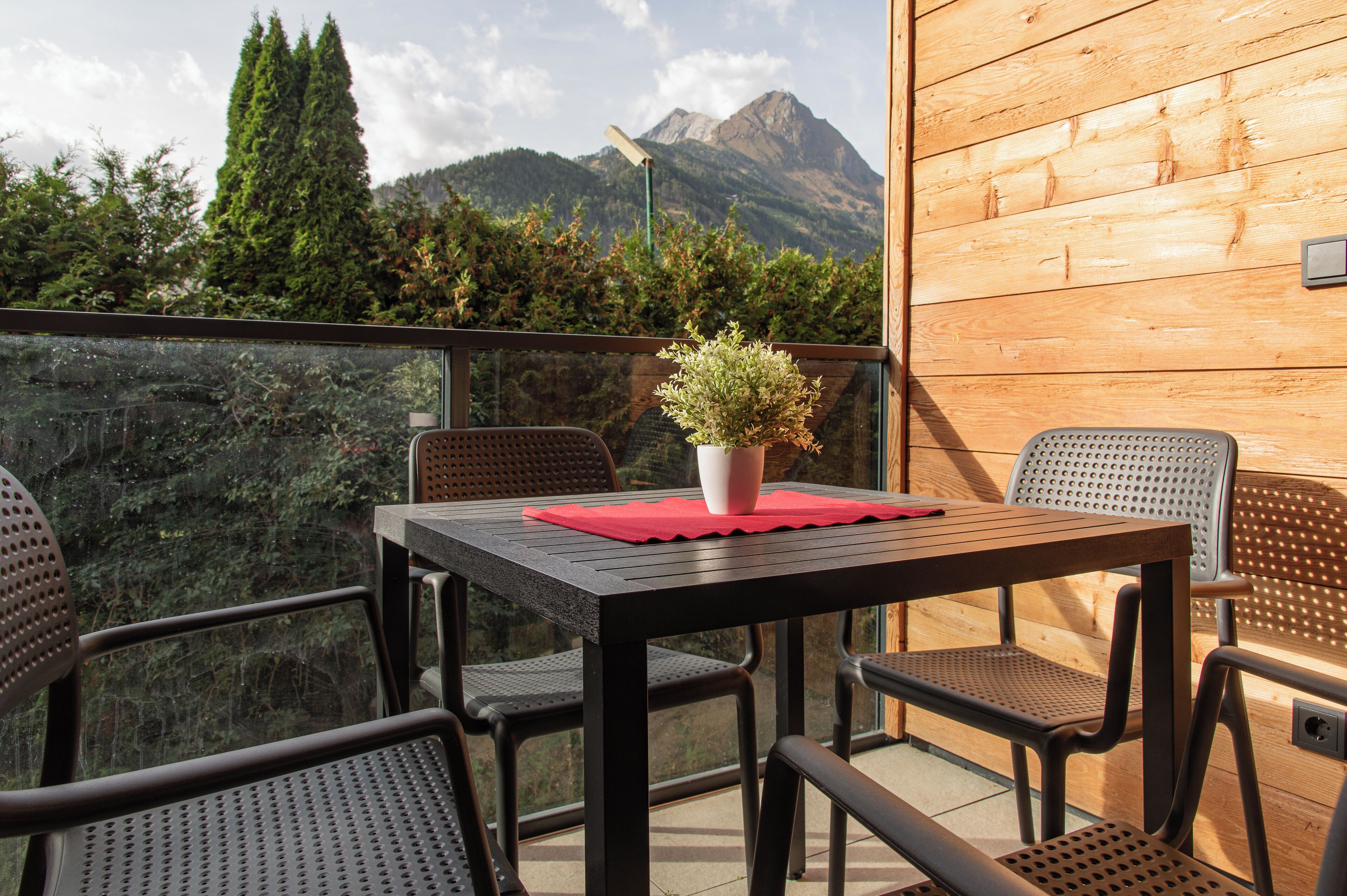 Een balkon met een tafel, stoelen, een bloempot en uitzicht op bergen.