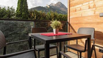 Een balkon met een tafel, stoelen, een bloempot en uitzicht op bergen.