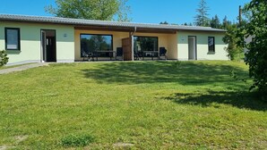 A modern building with a flat roof, large windows, and a covered outdoor seating area with tables and chairs. - Reihenhaus am Groß Labenzer See, Klein Labenz (Klein Labenz)
