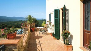 A terrace with potted plants, a table, and chairs, overlooking a scenic landscape.
