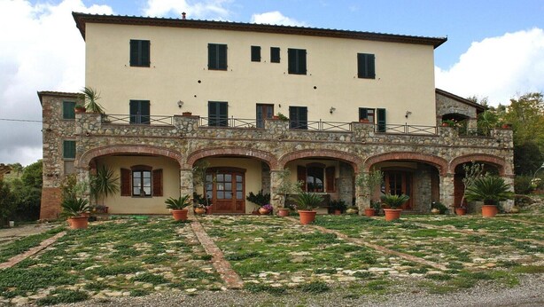 A two-story building with a stone facade, multiple windows, and a paved courtyard with potted plants.