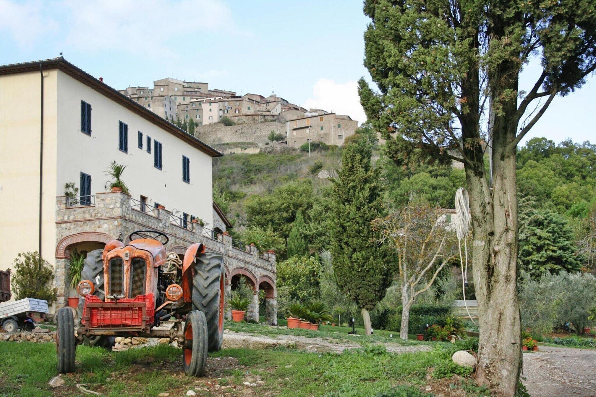 A rural setting with a white building, a red tractor, and a hill with buildings in the background.