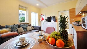 Un salon avec un canapé, une table à manger agrémentée d’un saladier de fruits, et un coin cuisine équipé d’un four à micro-ondes.
