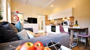 Un salon moderne comprenant un canapé, un coin repas avec une table et des chaises, une cuisine équipée et un téléviseur.
