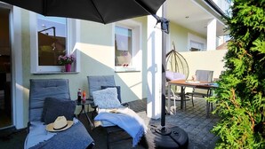 Une terrasse extérieure avec deux fauteuils de jardin, une table et un fauteuil suspendu.